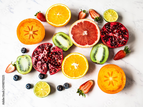Fototapeta Naklejka Na Ścianę i Meble -  Multicolored seasonal healthy natural fruit composition with persimmon, blueberries, orange, kiwi, strawberries, grapefruit, pomegranate, orange slices.