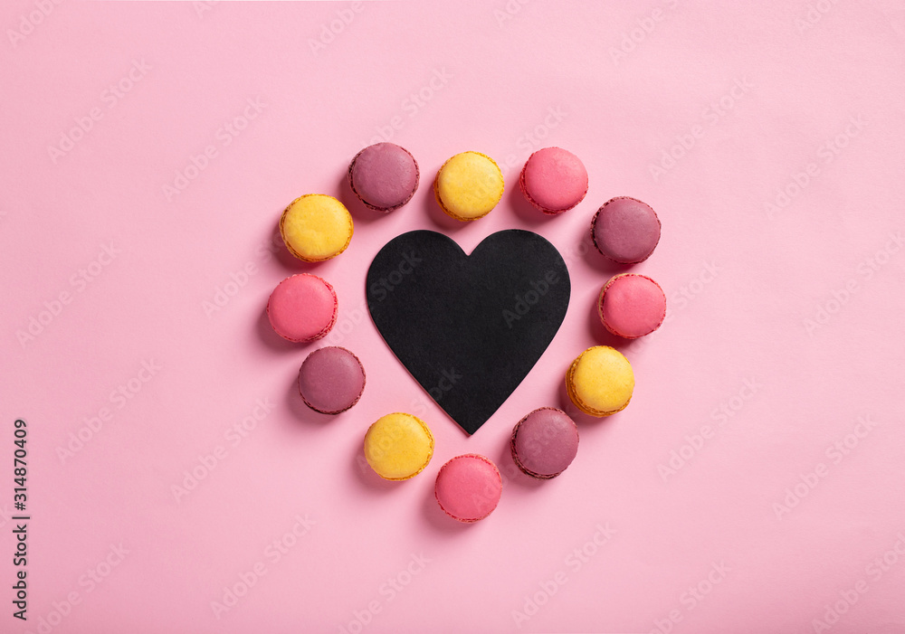 heart shape of colorful macarons around Valentine card with space for text. pink background. flat lay, minimal design.