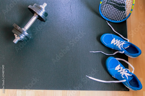 Blaue Sportschuhe auf Isomatte mit schwerer Hantel und Tennisschläger zeigt Fitness und Training zu Hause für körperliche Fitness, Gewichtsverlust, Fettabbau und Muskelaufbau im Fitnessstudio Zuhause