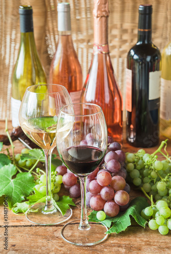 Winetasting concept. Two glasses of red and white wine, many different bottles of wine and ripe grapes on old wooden background. Vertical picture