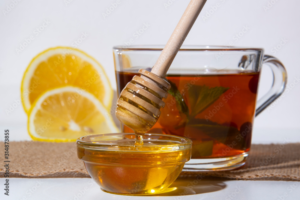 Honey with flowing from sticks in a bowl on the background of a cup of tea and lemon Honey with flowing from sticks in a bowl on the background of a cup of tea and lemon