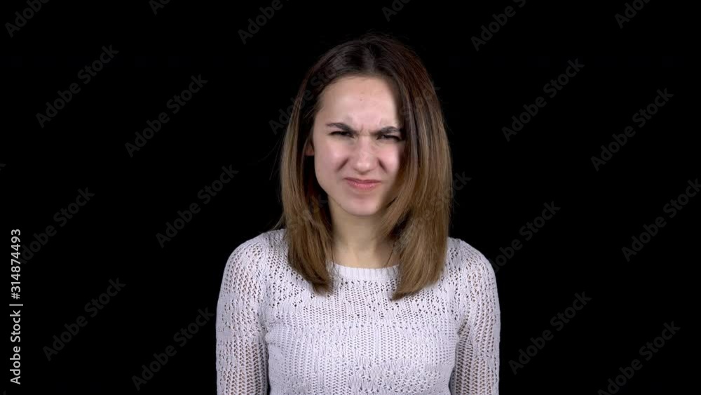 A young woman shows emotions of anger on her face. Woman screams in anger on a black background. A young woman shows emotions of anger on her face. Woman screams in anger on a black background.