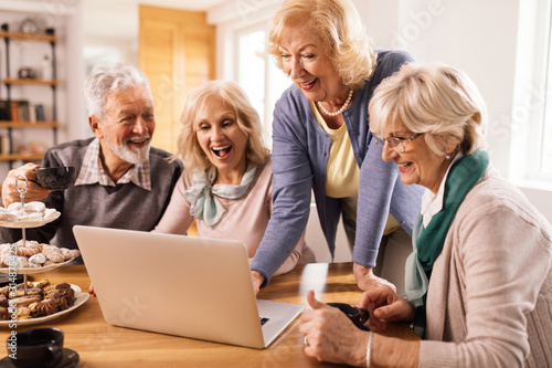 Group of happy seniors surfing the net on laptop at home.