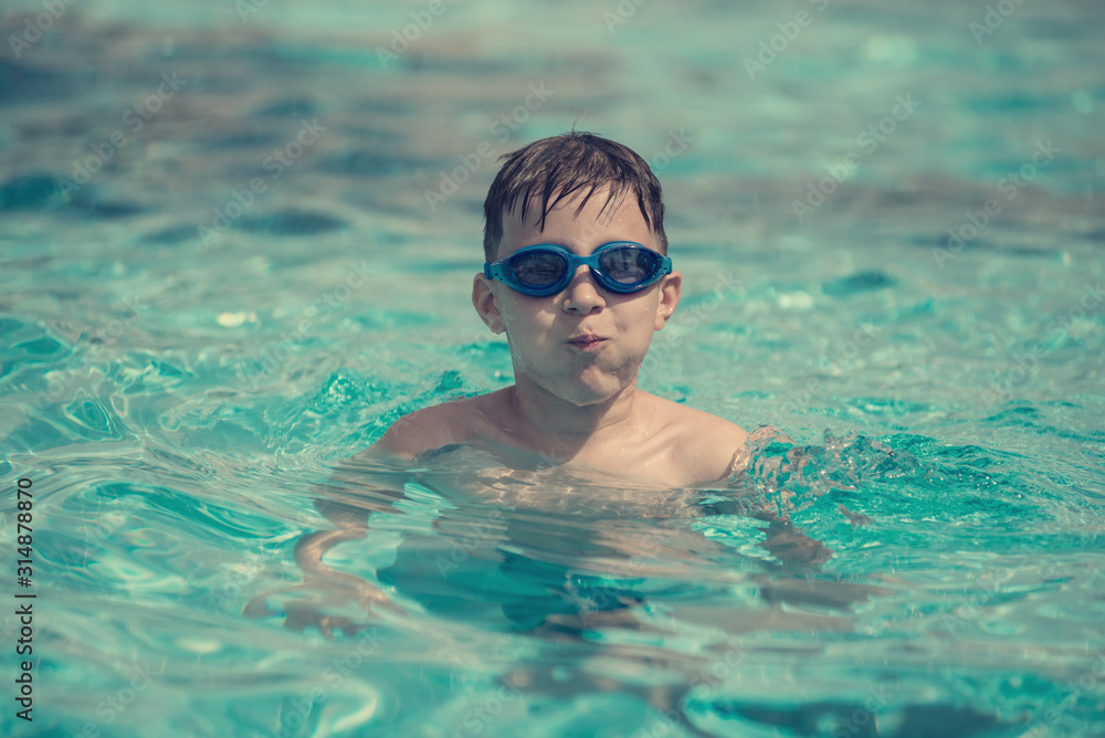 Naklejka premium The portrait of the cute European boy in swimming goggles in hotel’s swimming pool. He is enjoying his summer holidays.