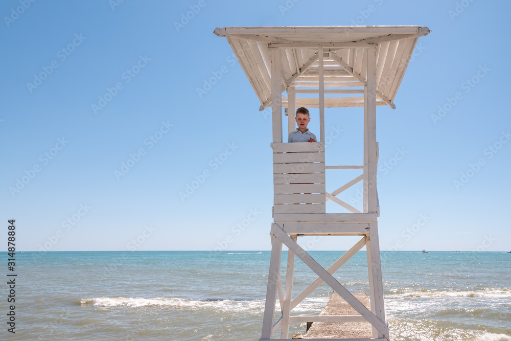 The boy stands in a rescue tower on the beach