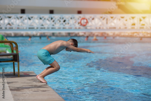 Caucasian boy spending time in pool at resort. He is making high jump to dive into swimming pool.