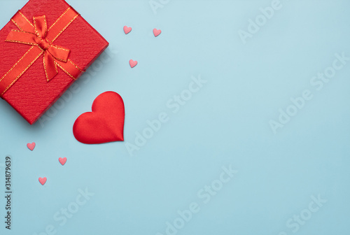 Romantic concept for Valentine`s Day. Flat lay. Pattern of pink and red hearts with red gift box on a blue background. Romantic concept. Copy Space
