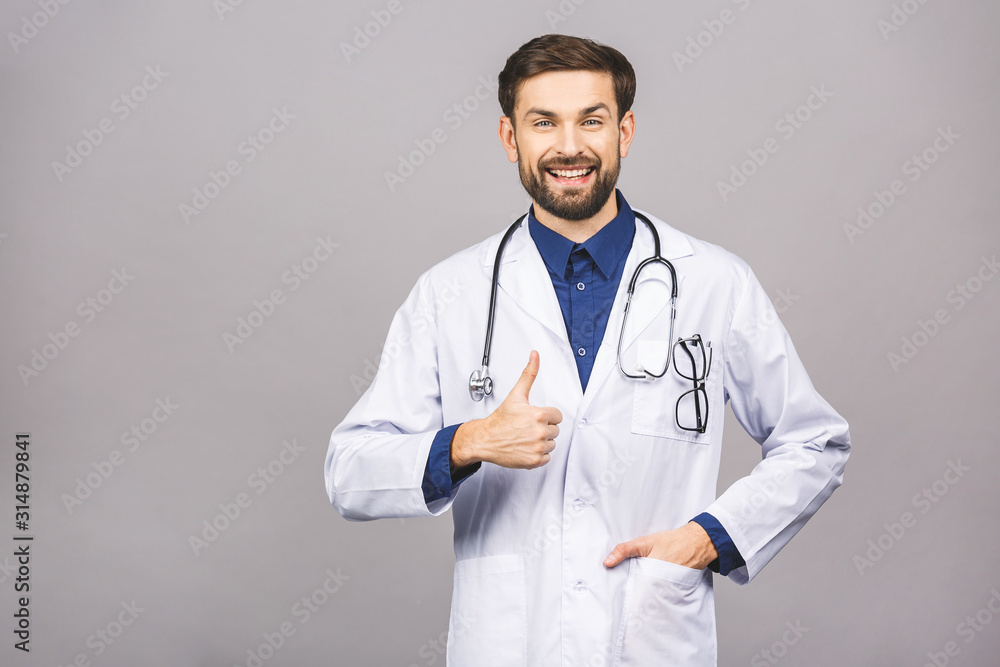 Portrait of cheerful smiling young doctor with stethoscope over neck in medical coat standing against isolated gray background. Thumbs up. Portrait of cheerful smiling young doctor with stethoscope over neck in medical coat standing against isolated gray background. Thumbs up.
