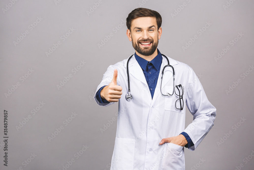 Portrait of cheerful smiling young doctor with stethoscope over neck in medical coat standing against isolated gray background. Thumbs up. Portrait of cheerful smiling young doctor with stethoscope over neck in medical coat standing against isolated gray background. Thumbs up.