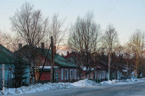 Small wooden houses on a street of Rabocheostrovsky, Karelia, Russia, in winter at sunset.