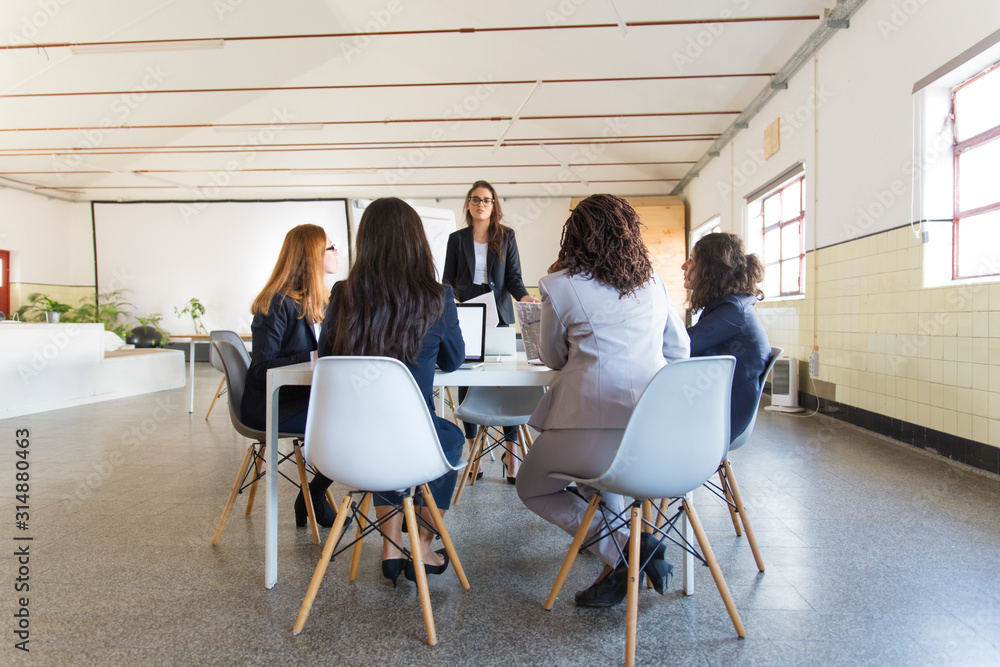 Coworkers sitting around table and looking at speaker. Group of professional multiethnic businesswomen looking at leader during meeting in office. Women in business concept Coworkers sitting around table and looking at speaker. Group of professional multiethnic businesswomen looking at leader during meeting in office. Women in business concept
