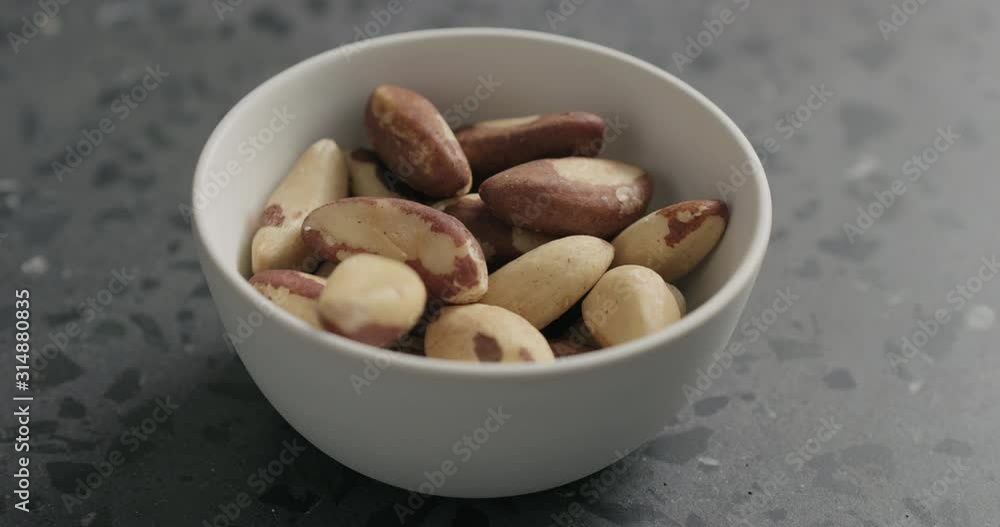 Slow motion brazil nuts falling into white bowl on terrazzo countertop Slow motion brazil nuts falling into white bowl on terrazzo countertop