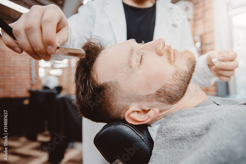 Hairdresser barber is holding razor for beard, male client is sitting in chair