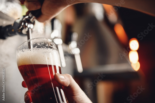 Bartender pours craft drink beer from tap into glass, dark background photo