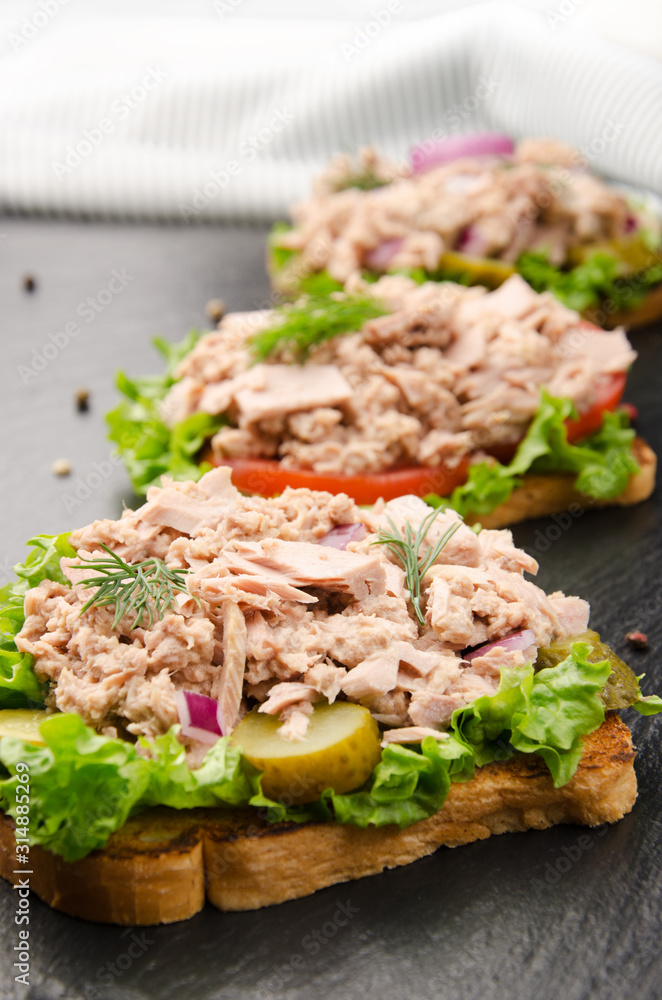 Tuna sandwiches with lettuce tomatoes pickles and onions on slate Tuna sandwiches with lettuce tomatoes pickles and onions on slate