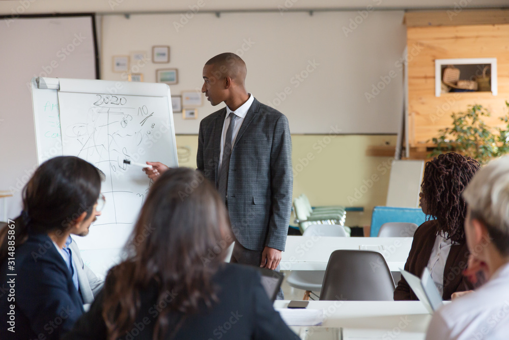 Thoughtful speaker pointing at whiteboard. Group of employees discussing ideas during presentation of new project at briefing. Business meeting concept Thoughtful speaker pointing at whiteboard. Group of employees discussing ideas during presentation of new project at briefing. Business meeting concept