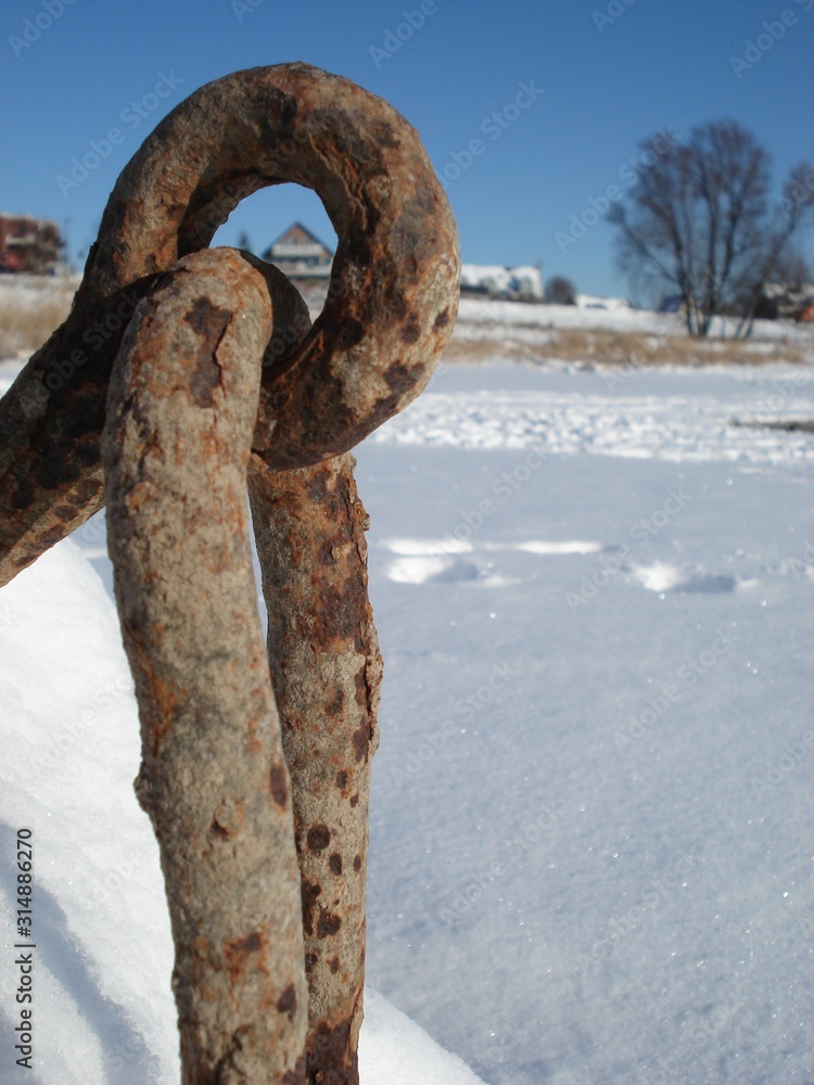 Schneebedeckte Landschaft mit rostigem Haken für ankernde Schiffe am Flussufer zeigt den Winter am sonnigen Tag von seiner schönsten Seite Schneebedeckte Landschaft mit rostigem Haken für ankernde Schiffe am Flussufer zeigt den Winter am sonnigen Tag von seiner schönsten Seite