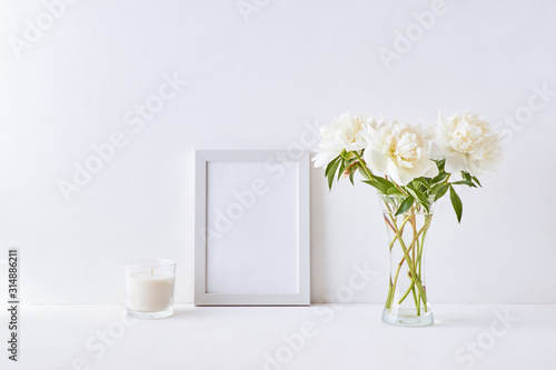 Mockup with a white frame and white peonies in a vase on a white background