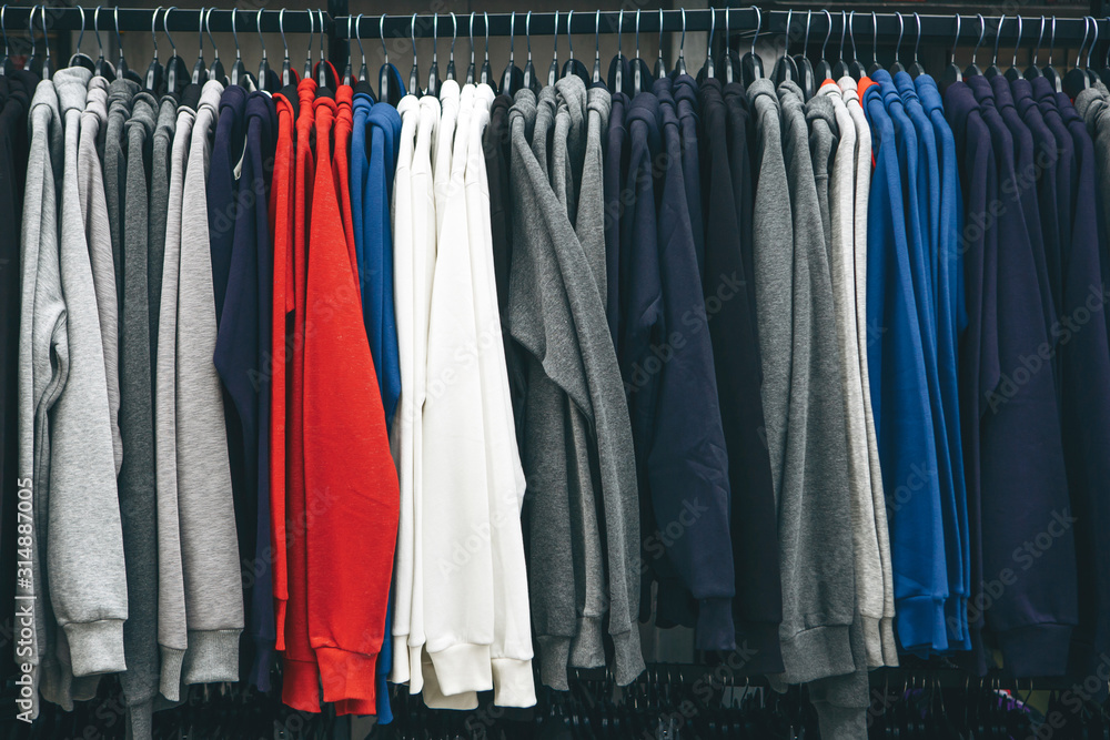 Many sweatshirts or pullovers hang on a hanger in a store or closet. A varied wardrobe and a selection of clothes