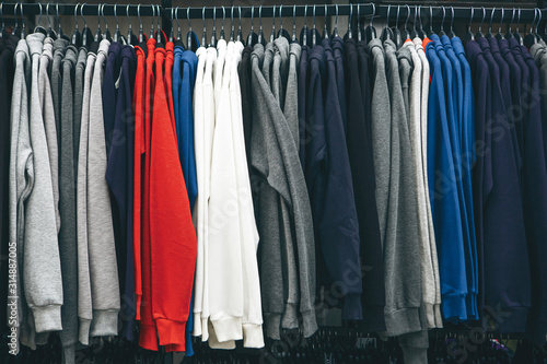 Many sweatshirts or pullovers hang on a hanger in a store or closet. A varied wardrobe and a selection of clothes