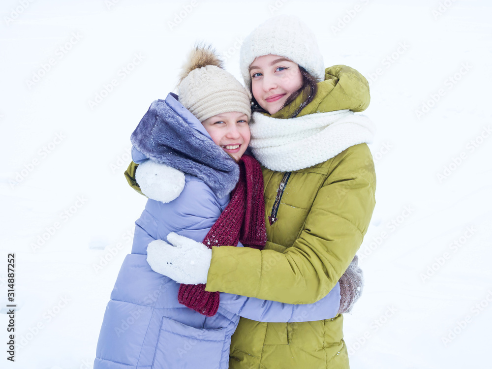 Two girls in colored down jackets are looking at the camera hugging in the winter. Winter clothes