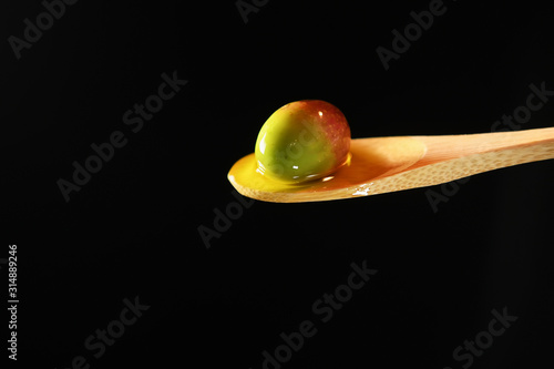 An olive in olive oil on a wood spoon in extra virgin olive oil on a black background