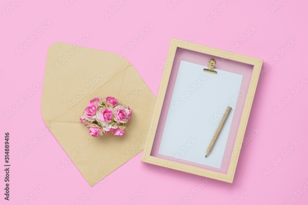 Mockup photo frame with Kraft rose flower in brown envelope for Valentines day concept. Top view of mock up photo frame with craft decoration and on pastel pink background. Flat lay with copy space. Mockup photo frame with Kraft rose flower in brown envelope for Valentines day concept. Top view of mock up photo frame with craft decoration and on pastel pink background. Flat lay with copy space.
