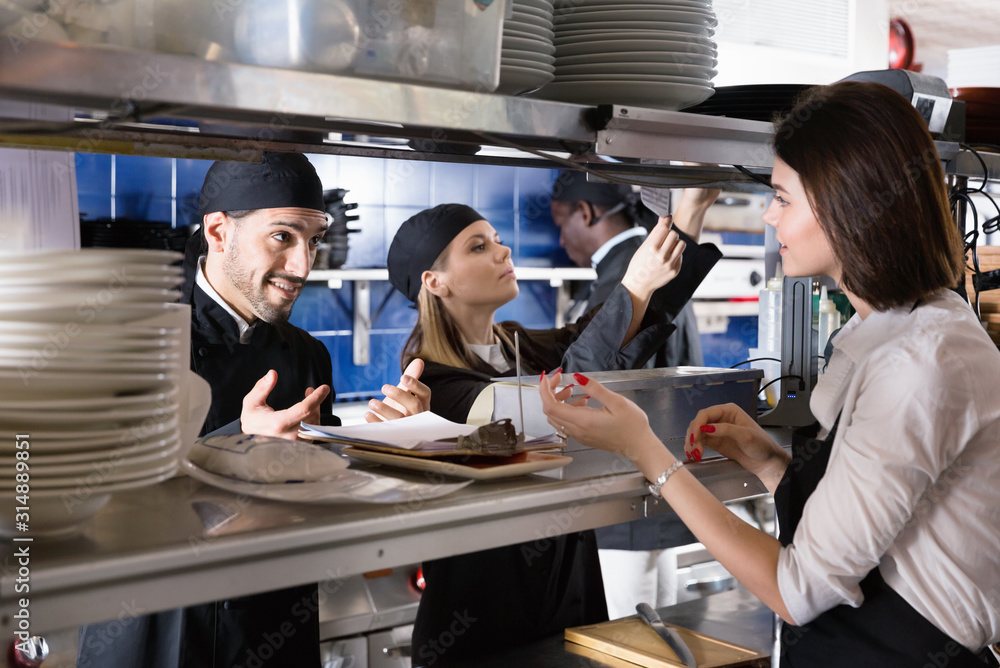 © JackF - Woman waiter is giving order to chef cook on kitchen in restaurant.