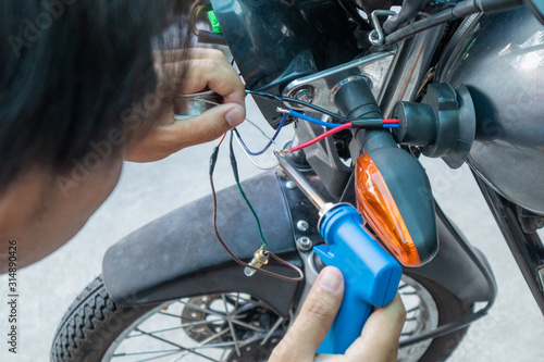 Asian young man fix and welding wire motorcycle lamp in garage. safety and check motorcycle. checking motorcycle before riding travel. Repair or maintanance concept. photo