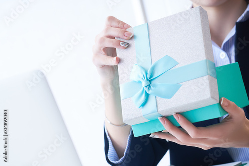 Christmas, any holiday. Office employee received a gift from her colleagues. Closeup woman hands holds gift box on office background.