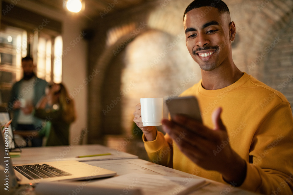 Happy black freelancer using smart phone while working in the evening at the office. Happy black freelancer using smart phone while working in the evening at the office.