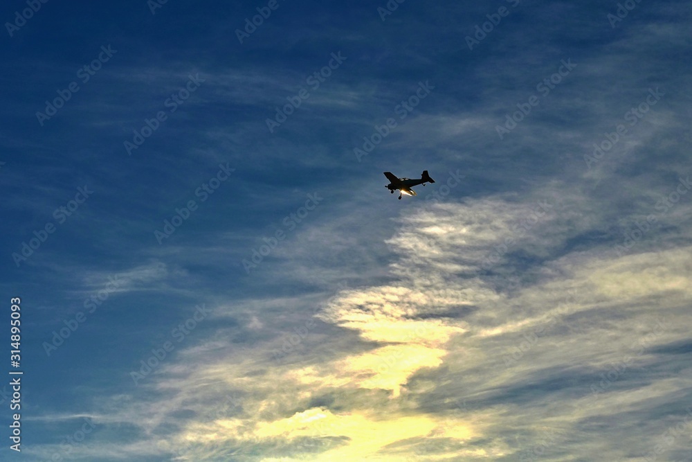 Small airplane on blue sky with clouds and sunset in background
