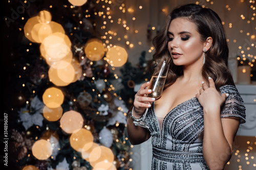 Party, drinks, holidays, luxury and celebration concept - smiling woman in evening dress with glass of champagne over Christmas background.  Winter holiday. Lights around.