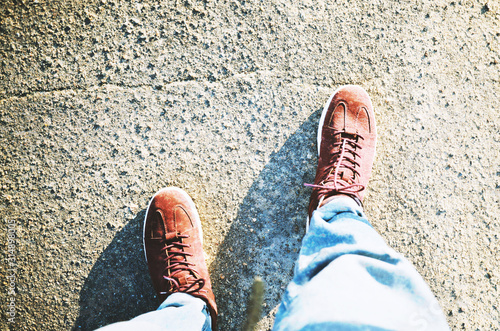Man in red sneakers and blue jeans walks along the asphalt road in the city