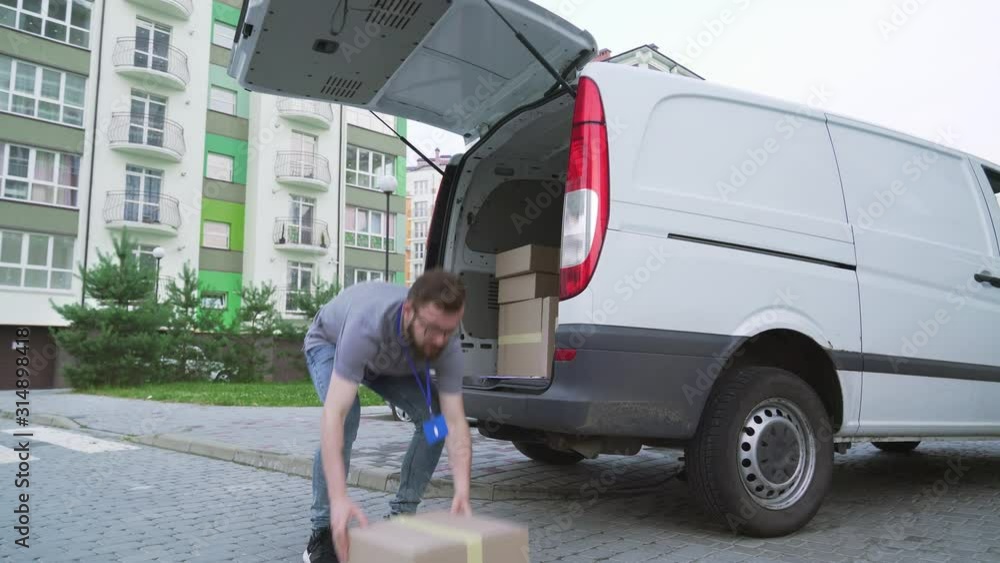 Handsome delivery man taking out parcels from car trunk Handsome delivery man taking out parcels from car trunk