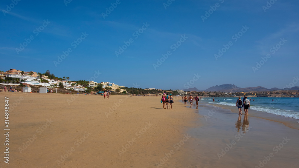Tourists strolling along the shallow-water beach, enjoying the tropical weather, the calm ocean, at this holiday destination, Costa Calma, Fuerteventura, Canary Islands, Spain