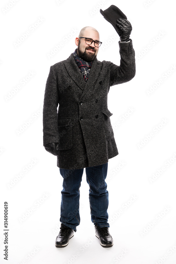 Elegant man with a beard in a coat and hat. He stands in full growth on a white background and holds on to his hat. Vertical. Elegant man with a beard in a coat and hat. He stands in full growth on a white background and holds on to his hat. Vertical.