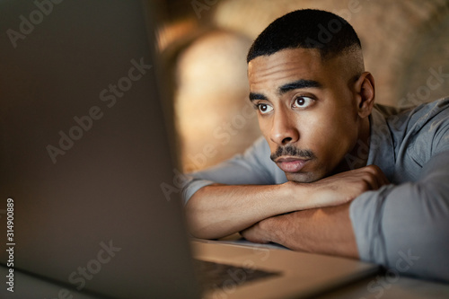 Young black entrepreneur reading e-mail on laptop at night.