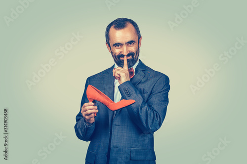 man holding a red shoe, showing hush hand gesture with finger