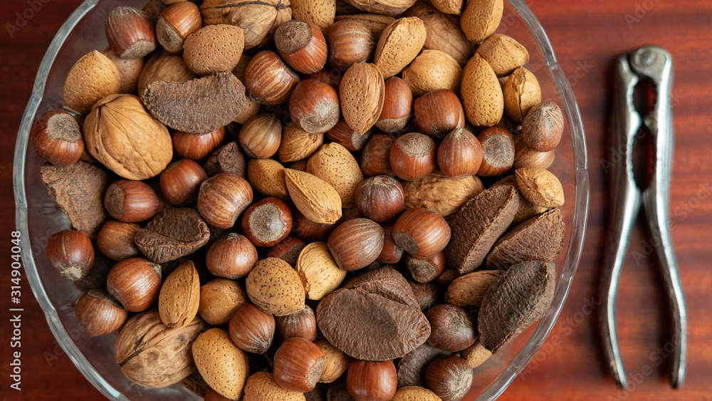 Assortment of whole nuts, walnuts, almonds, hazelnuts and Brazil nuts in a bowl with a nut cracker on a side, nutritious snack cracked and eaten in autumn or winter months as a special holidays treat. Assortment of whole nuts, walnuts, almonds, hazelnuts and Brazil nuts in a bowl with a nut cracker on a side, nutritious snack cracked and eaten in autumn or winter months as a special holidays treat.