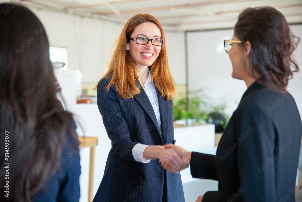 Smiling redhead businesswoman shaking hands with colleague. Cheerful female workers shaking hands in office. Handshake concept Smiling redhead businesswoman shaking hands with colleague. Cheerful female workers shaking hands in office. Handshake concept