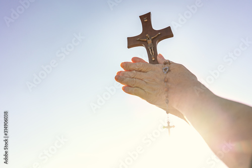 Woman praying outdoor with a crucifix with blinding sun light .