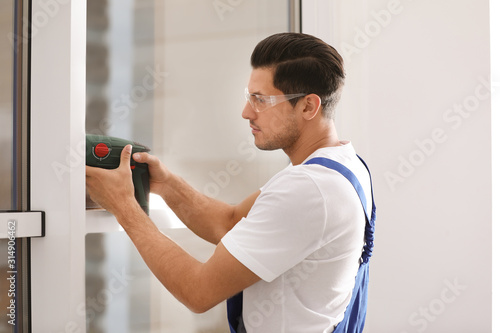 Construction worker repairing plastic window with electric screwdriver indoors