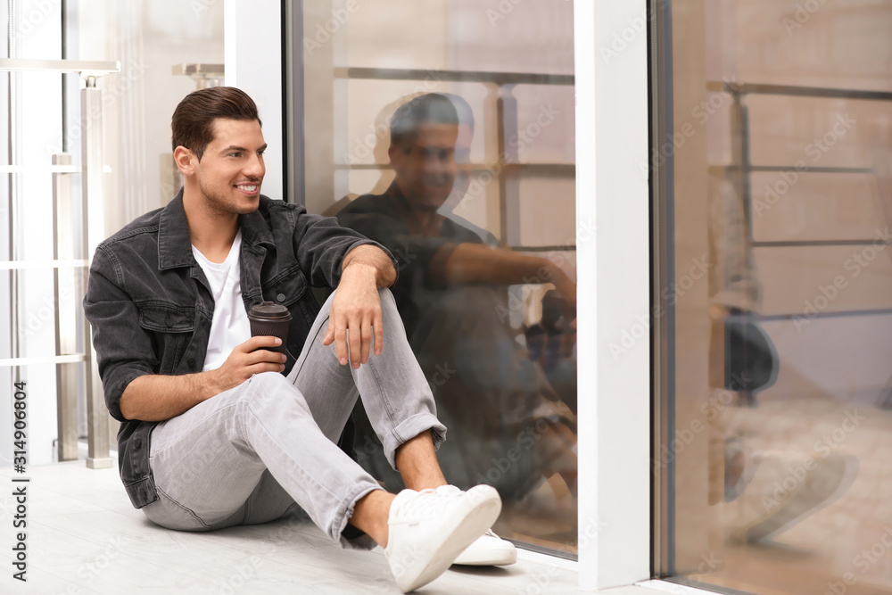 Handsome man with paper cup of coffee near window at home Handsome man with paper cup of coffee near window at home