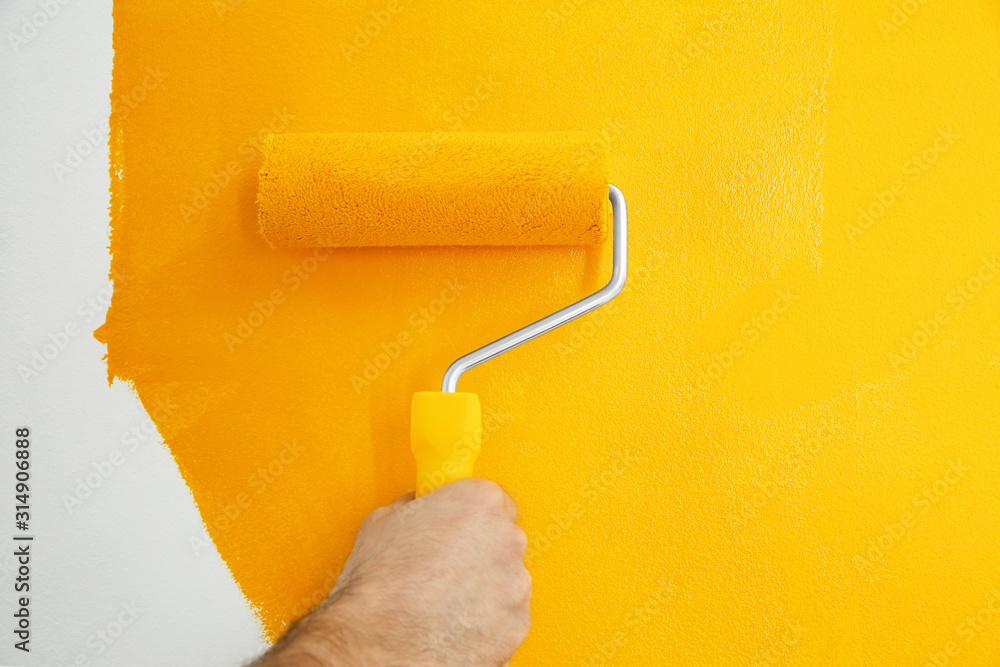 Obraz premium Man painting white wall with yellow dye, closeup. Interior renovation