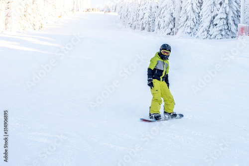 Young boy snowboarder riding snowboard down the hill in mountain ski resort