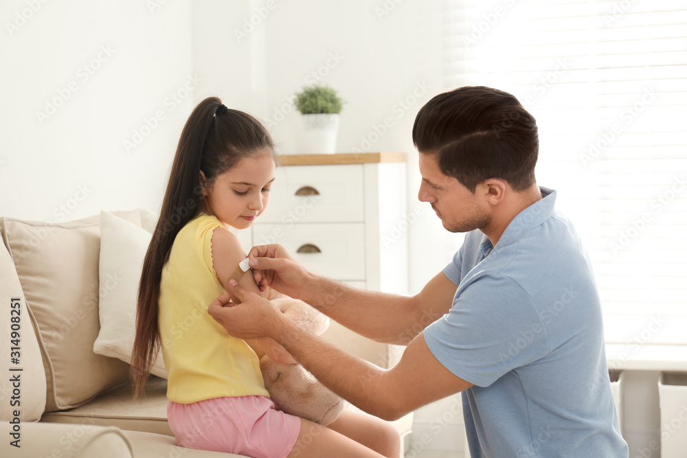 Father putting sticking plaster onto daughter's arm at home Father putting sticking plaster onto daughter's arm at home