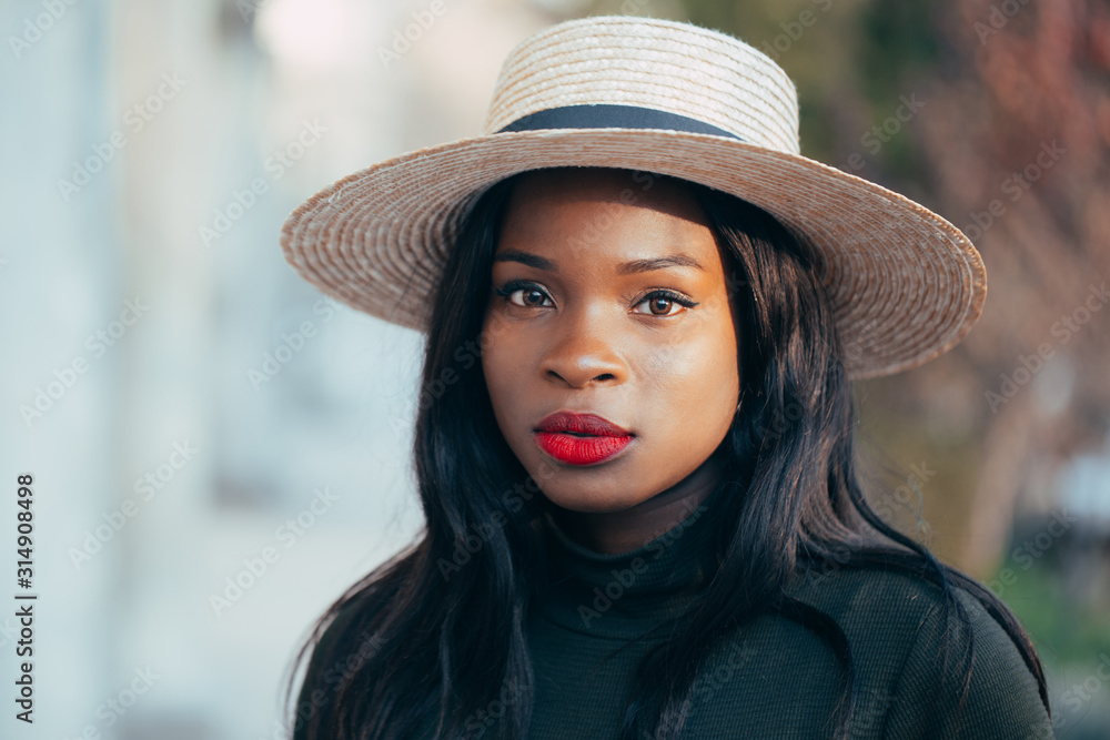 Beautiful young black african girl in a hat with a happy smile on the street in the rays of the setting autumn sun. close-up. Fashion colors