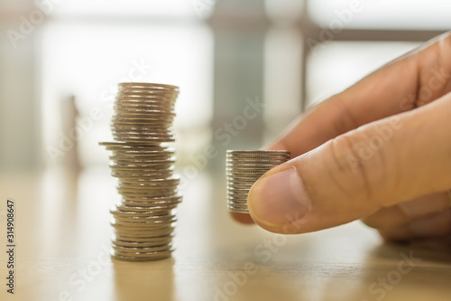 Business, Saving and Retirement concept. Close up of stack of coins in man hand putting down on wooden table near unstable stack of coins.