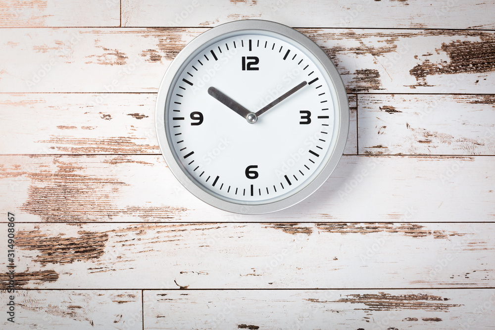White wall clock with a yellow used hanging on the wall. Minimalist image of a wall clock on a wooden background with copy space White wall clock with a yellow used hanging on the wall. Minimalist image of a wall clock on a wooden background with copy space